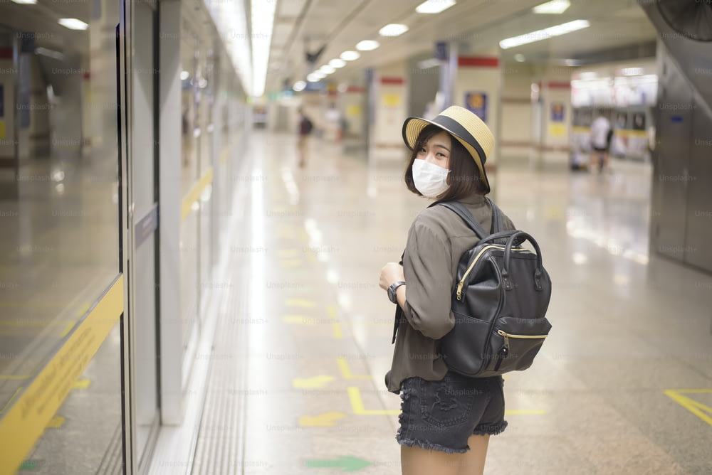 若いかわいいアジアの女性が地下鉄駅に立って保護マスクを着用しています、ニューノーマル旅行、covid-19保護、安全な旅行、COVID-19下での旅行、パンデミック後の旅行コンセプト。
