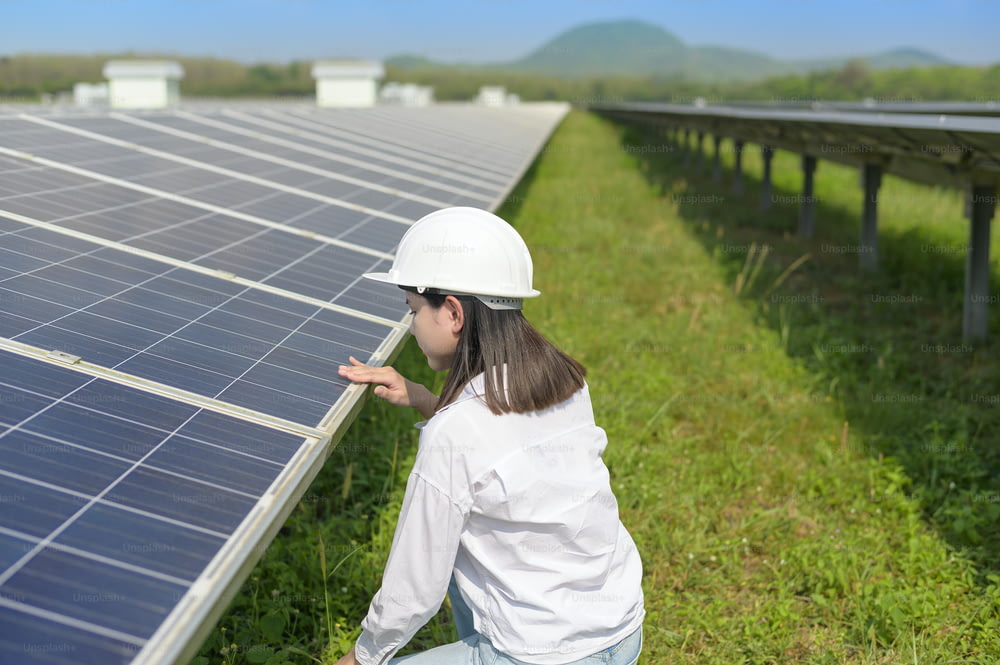 Une femme ingénieure portant un casque dans une ferme de cellules photovoltaïques ou un champ de panneaux solaires, une énergie écologique et propre.