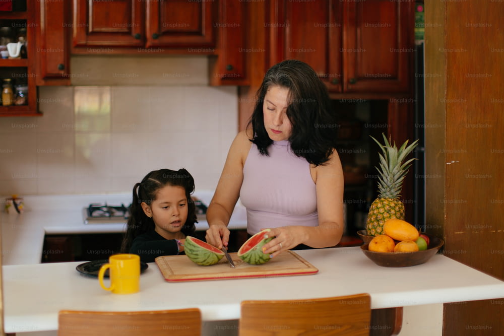 a woman and a little girl cutting up a watermelon
