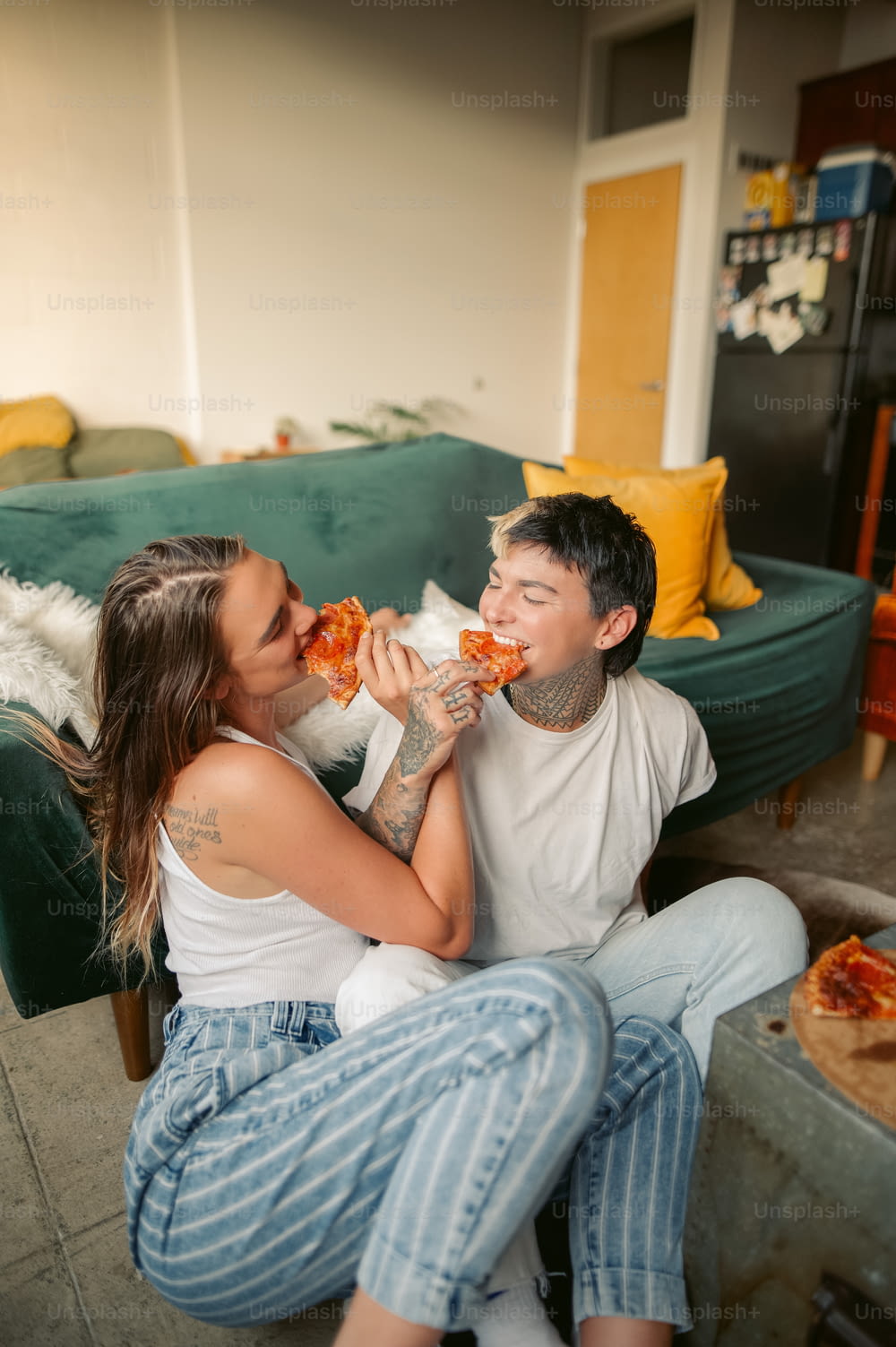 Un uomo e una donna seduti su un divano che mangiano pizza