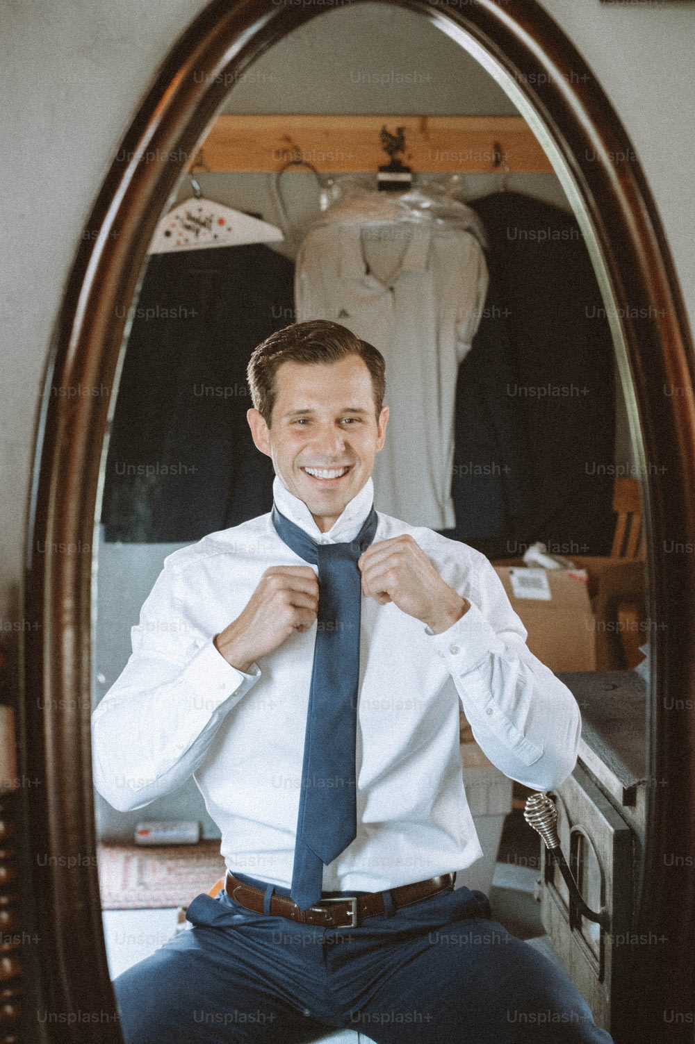 a man sitting in front of a mirror tying his tie
