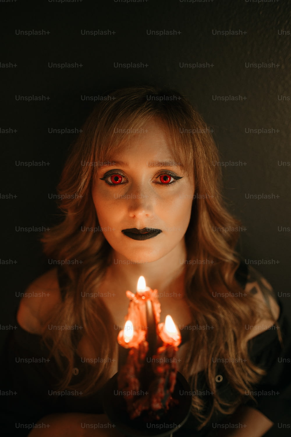 Una donna con gli occhi rossi che tiene una candela accesa
