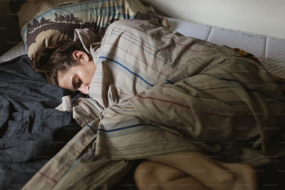 une personne dormant dans un lit avec une couverture