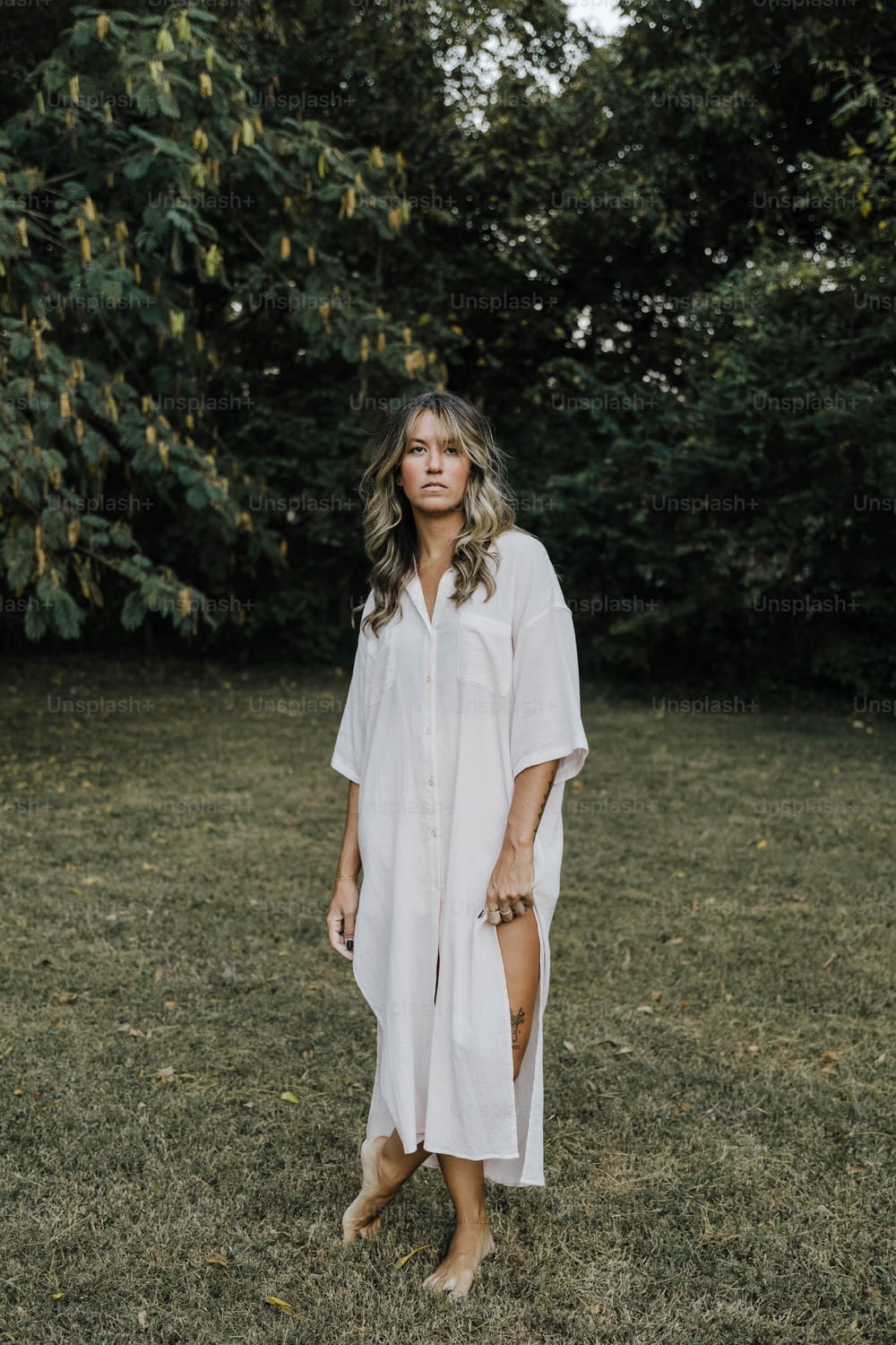 a woman standing in a field wearing a white shirt dress