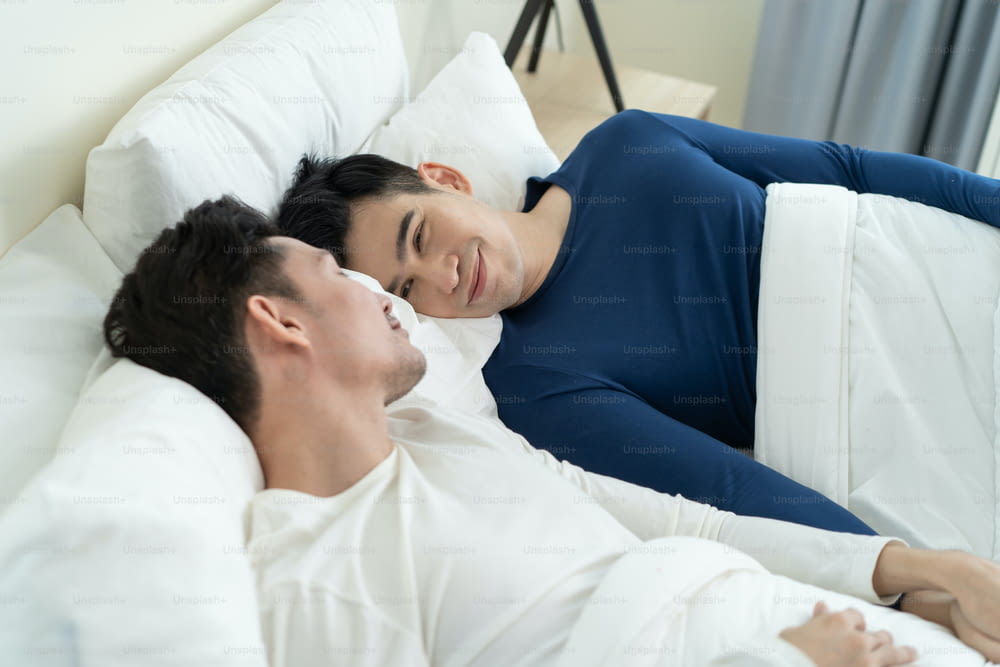 Casal gay de homem bonito asiático deitado na cama e olhar um para o outro. Atraente romântico masculino lgbt de pijama dormindo no início da manhã juntos no quarto em casa. Conceito homossexual-LGBTQ.