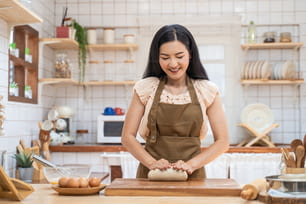 Mulher madura bonita asiática ficar em casa, passar o tempo na cozinha cozinhando. Jovem atraente carring feminino usar avental e sorriso, massa de levedura amassada com a mão para assar padaria na mesa para o jantar em casa
