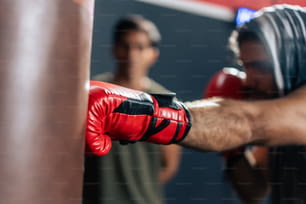 Homem caucasiano usa luvas de boxe socando à frente com treinador na academia. Atraente jovem fisiculturista boxe masculino malhando com a ajuda do belo treinador Asain para cuidados de saúde em finess ou ginásio.