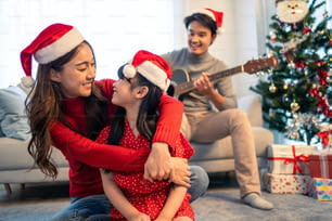 Un encantador miembro de la familia asiática disfruta cantando canciones navideñas juntos en casa. La pequeña hija se siente feliz y emocionada de celebrar la fiesta de Acción de Gracias navideña junto con los padres en casa.