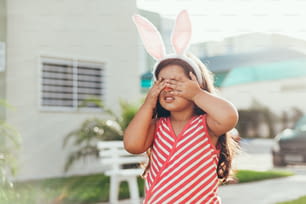 Menina bonita com orelhas de coelho e cesta de ovos de Páscoa no jardim. Caça aos ovos de Páscoa