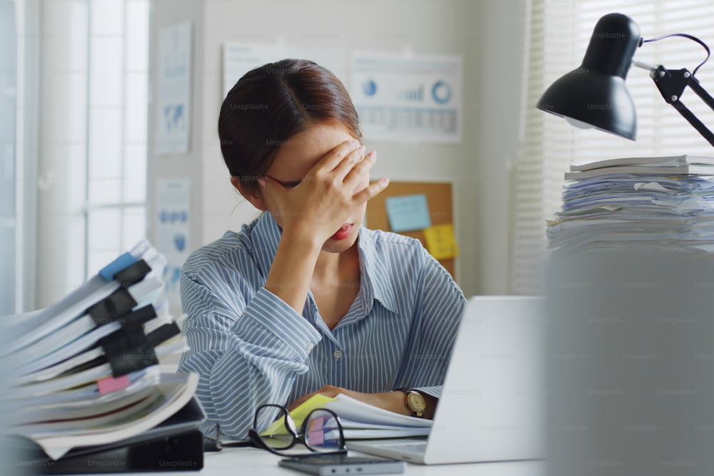 Versuchte junge asiatische Büroangestellte, die sich krank fühlen und Kopfschmerzen von einem langen Arbeitstag im Büro haben