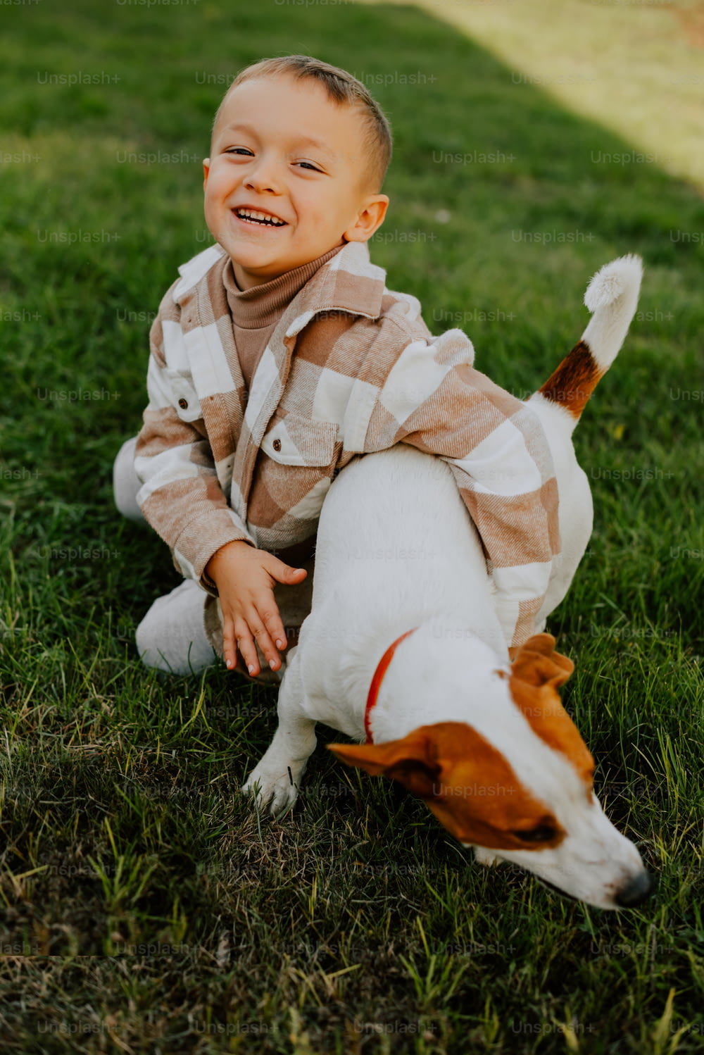 Un niño pequeño que está sentado en la hierba con un perro