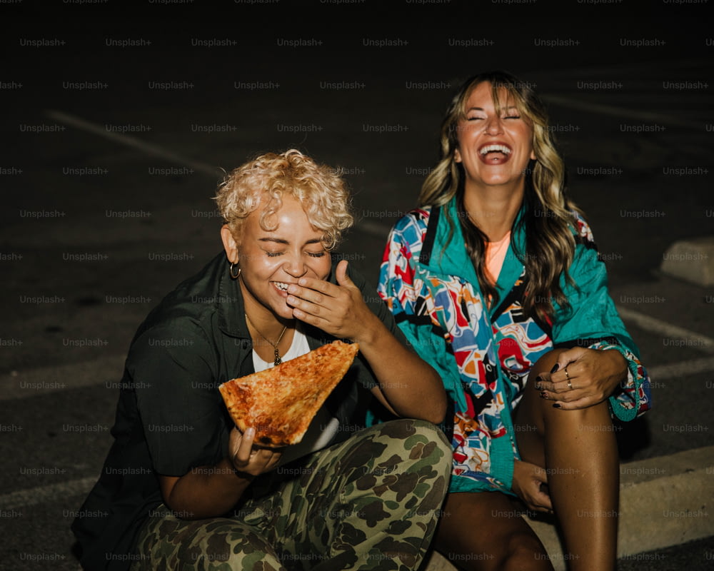 Un paio di donne sedute una accanto all'altra mangiano una fetta di pizza