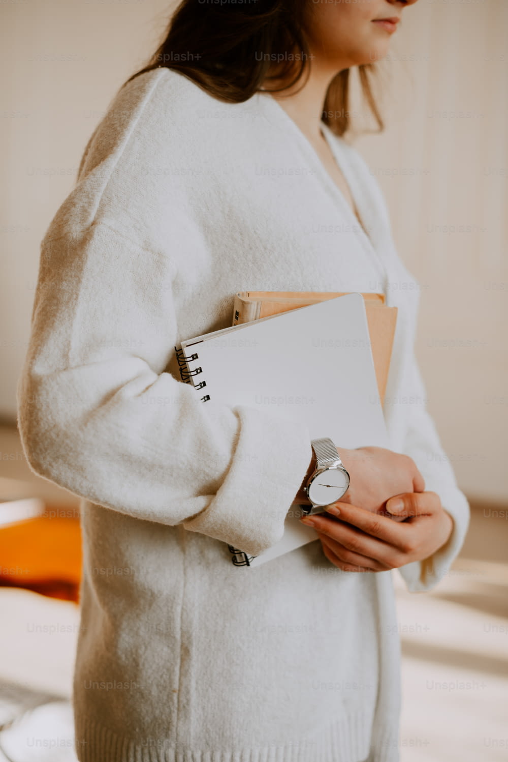 uma mulher de camisola branca a segurar um caderno e um relógio