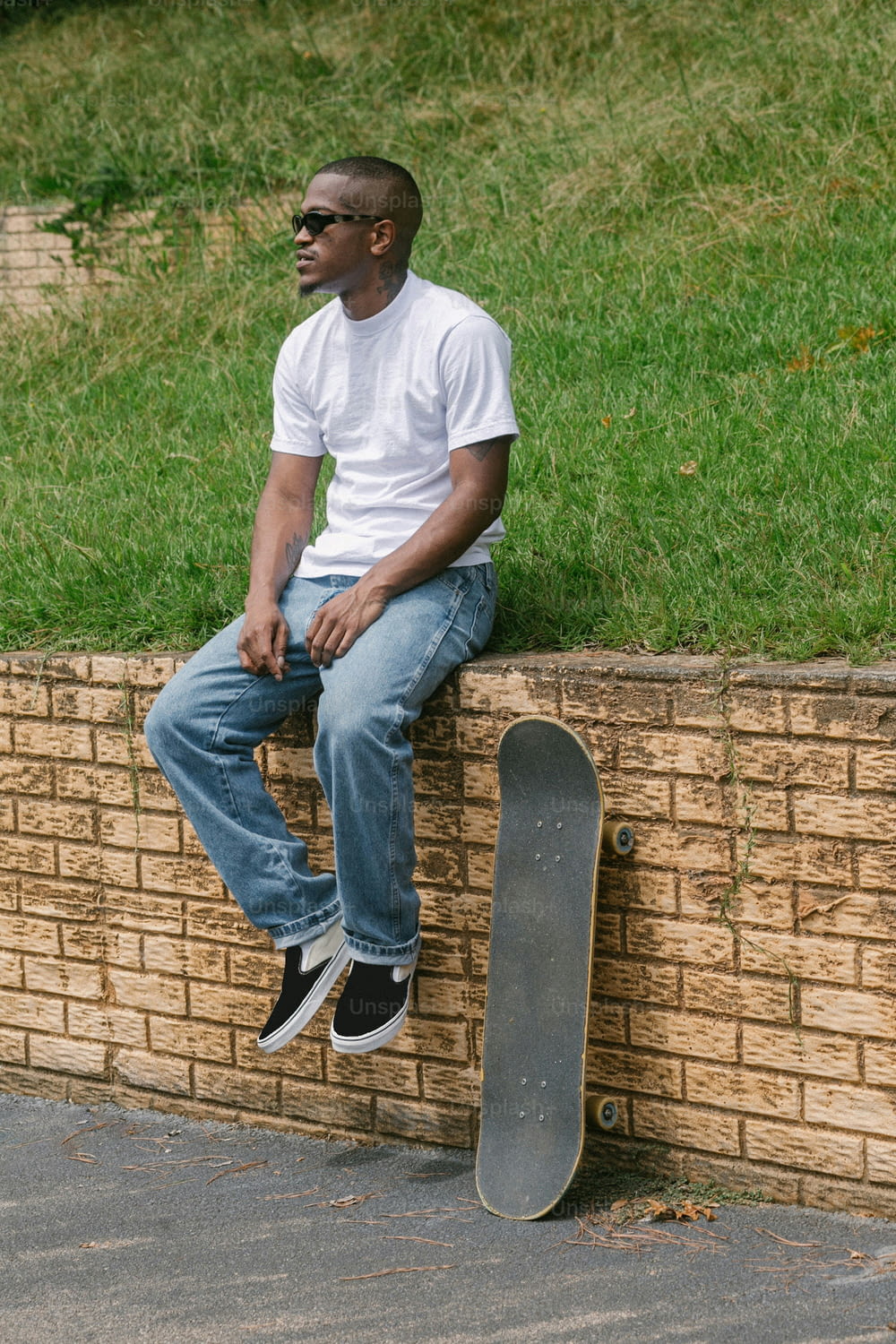 Ein Mann, der mit einem Skateboard auf einer Ziegelmauer sitzt