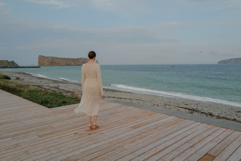 a woman standing on a wooden deck near the ocean