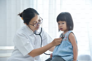 젊은 아시아 여성 의사가 청진기로 어린 소녀를 검사하고 있다. 의학 및 건강 관리 개념입니다.