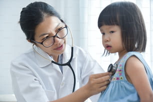 젊은 아시아 여성 의사가 청진기로 어린 소녀를 검사하고 있다. 의학 및 건강 관리 개념입니다.