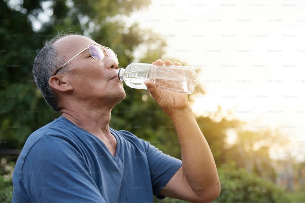 Asian senior male drinking water after exercise at park outdoor background.