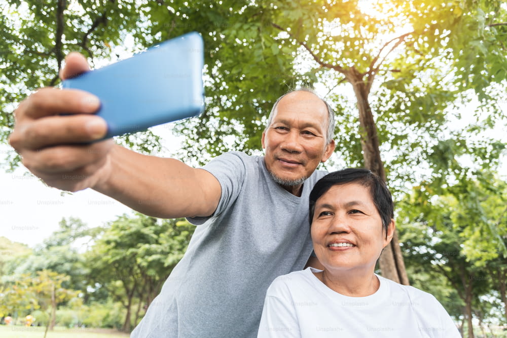 Asian Senior Couple taking selfie photos with smartphone at park outdoor. Smiling face.