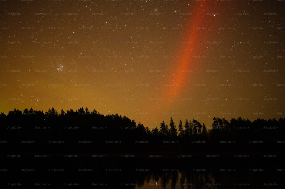 Una luz naranja brillante brilla en el cielo nocturno sobre un lago
