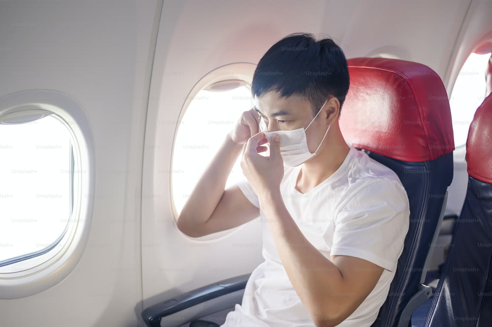 Um homem que viaja está usando máscara de proteção a bordo da aeronave, viajando sob a pandemia de Covid-19, viagens de segurança, protocolo de distanciamento social, Novo conceito de viagem normal