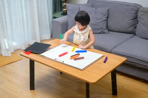 Baby girl drawing with colored pencils in living room at home.
