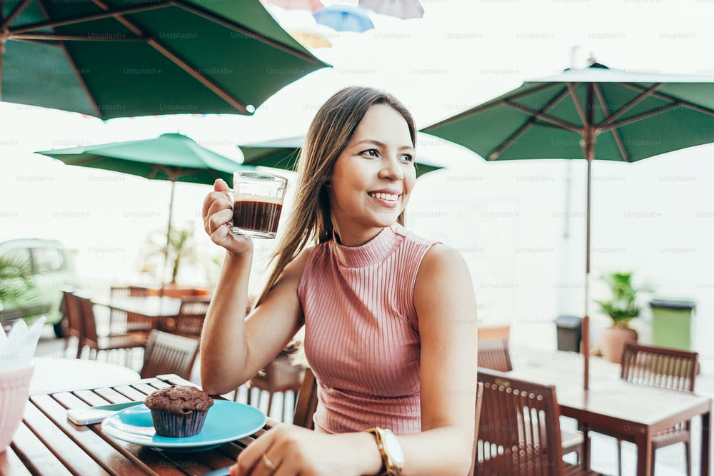 Young woman having a breakfast with coffee and cake sitting outdoors in a cafe