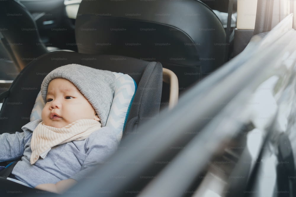 Retrato do bebê recém-nascido asiático bonito sentado em seu assento de segurança do carro no carro enquanto viajava.