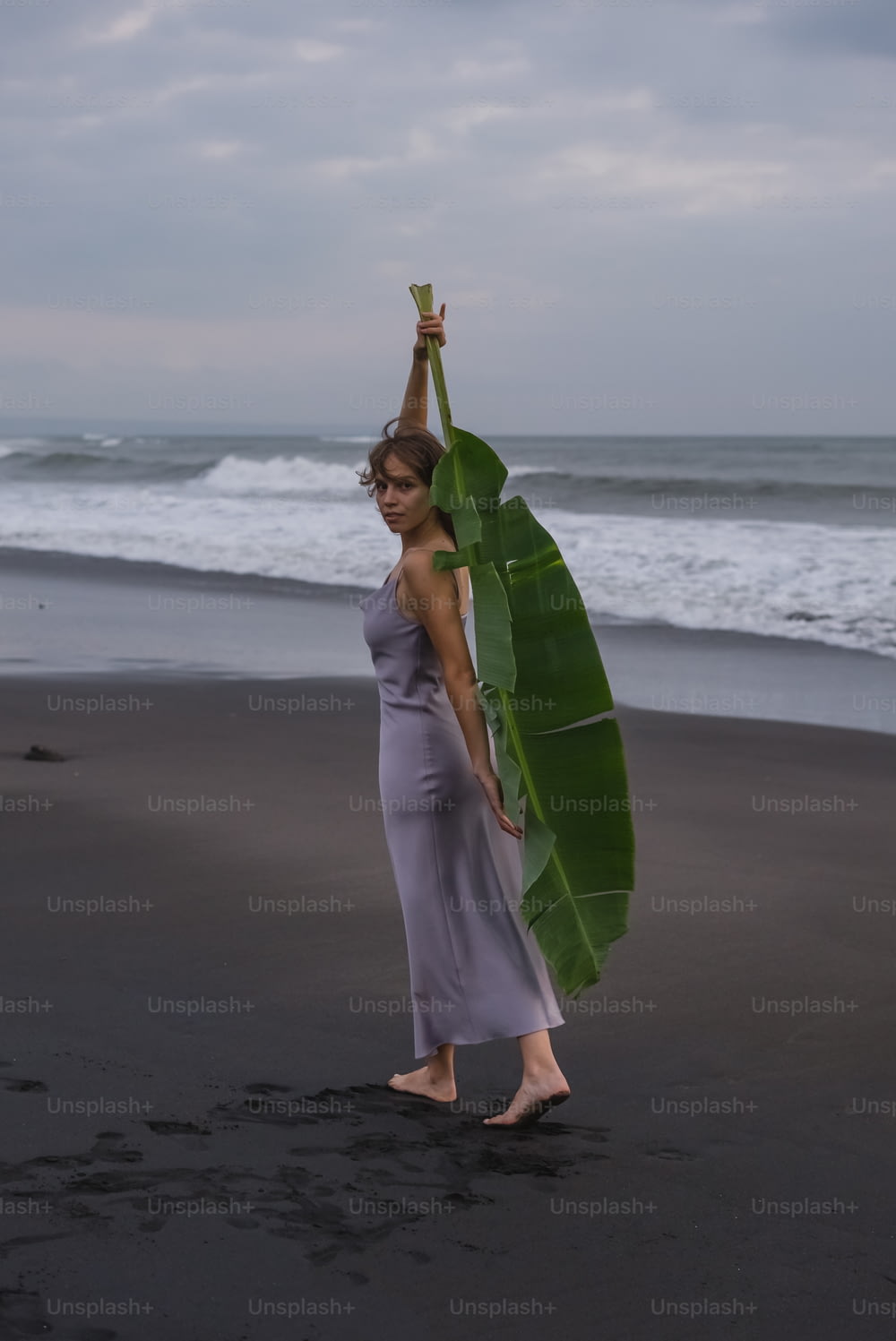 uma mulher segurando uma grande folha de bananeira em uma praia