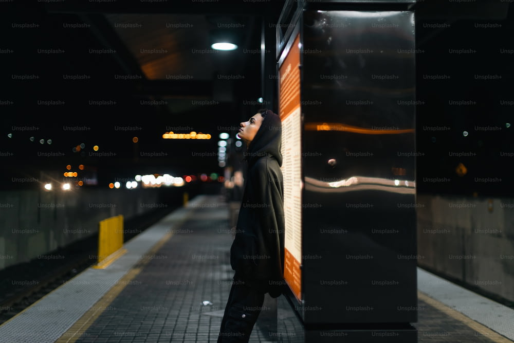 a woman leaning against a wall on a train platform
