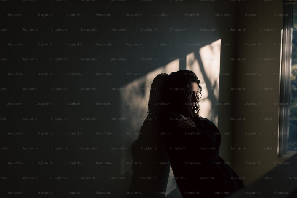 窓際の暗い部屋に立つ女性