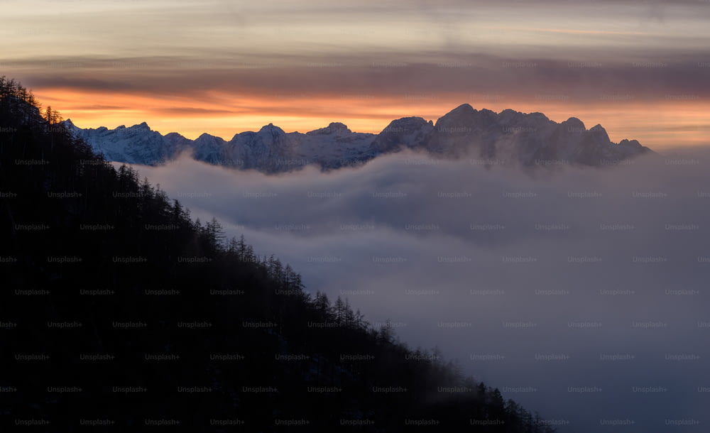 uma montanha coberta de nevoeiro e nuvens ao pôr do sol
