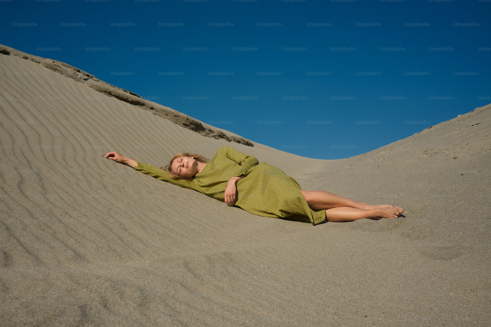 a woman in a green dress laying in the sand