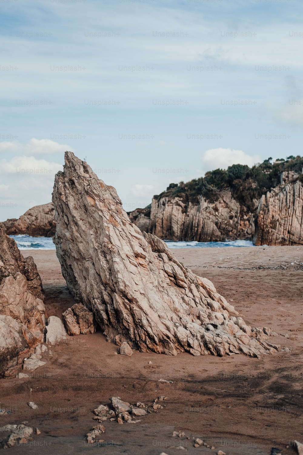 un gros rocher assis au sommet d’une plage de sable