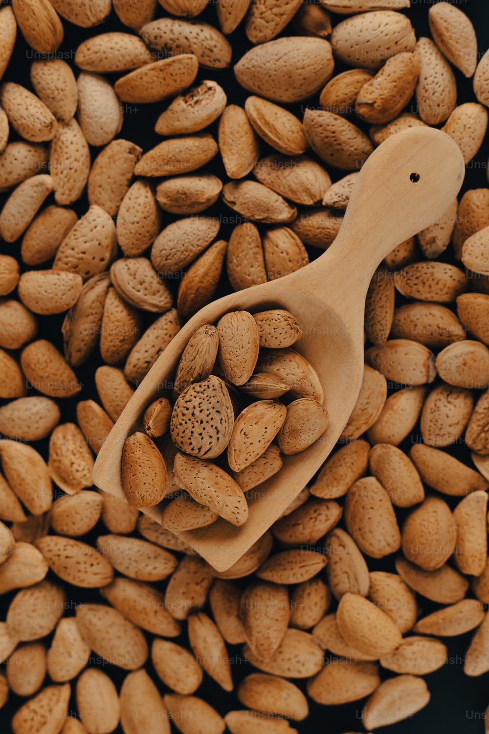 un cucchiaio di legno pieno di arachidi sopra un mucchio di arachidi