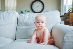 um bebê sentado em um sofá com um relógio ao fundo