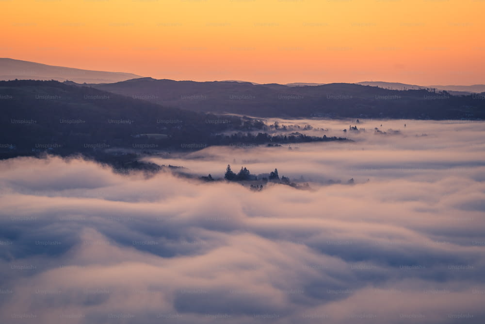 a view of a valley covered in clouds at sunset