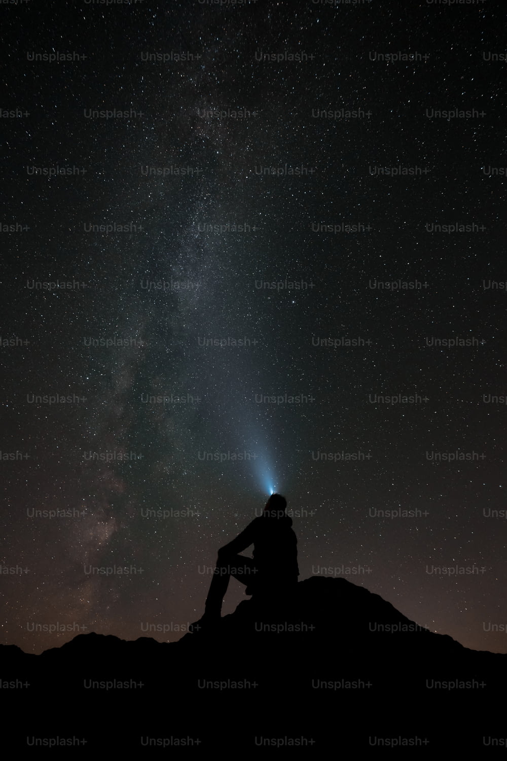 Un uomo seduto sulla cima di una collina sotto un cielo notturno pieno di stelle