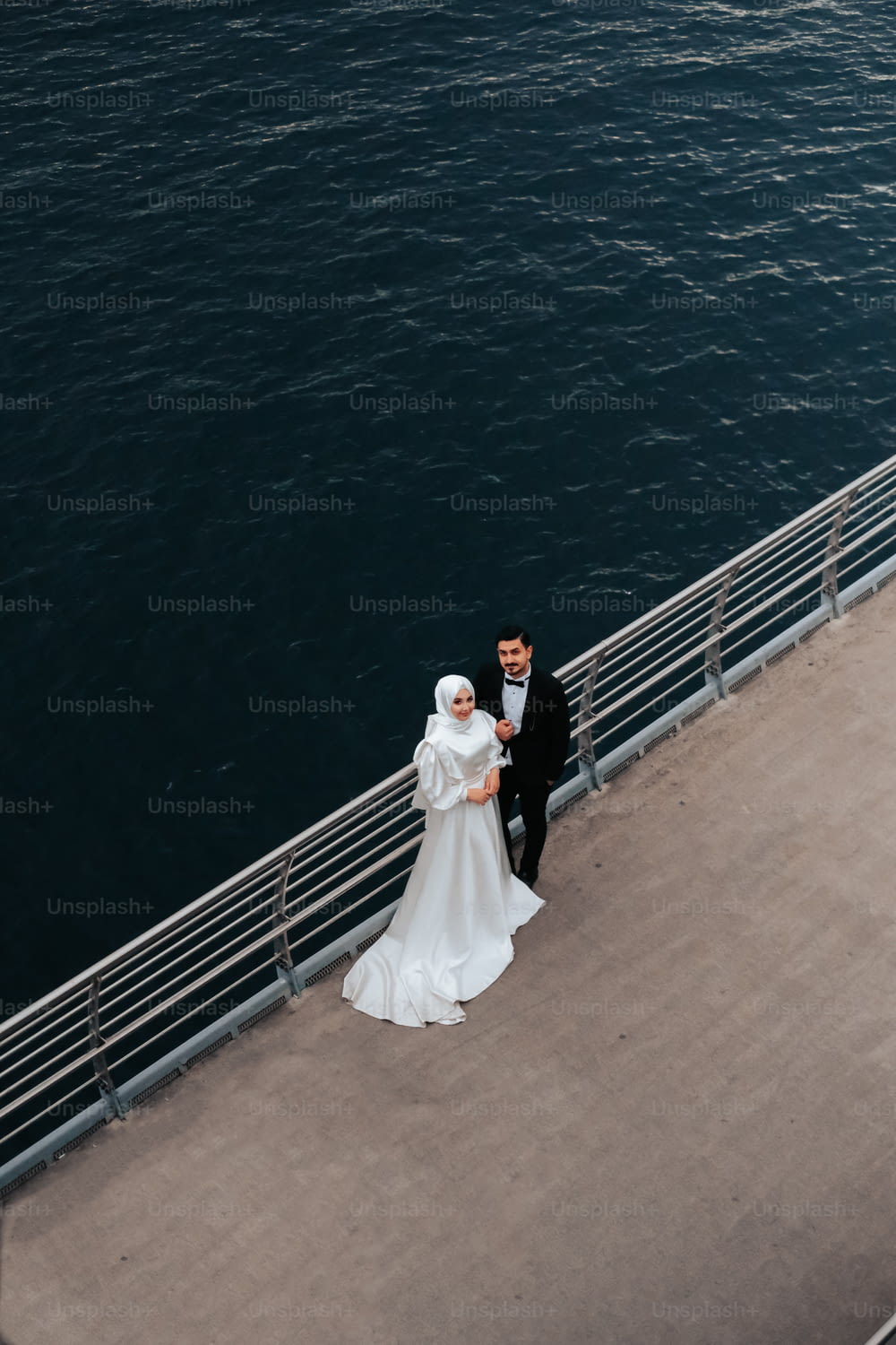 Una sposa e uno sposo in piedi su un molo vicino all'acqua