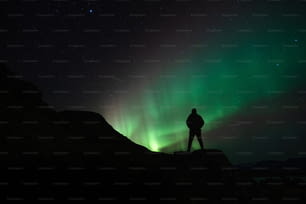 Una persona parada en una montaña mirando la aurora boreal