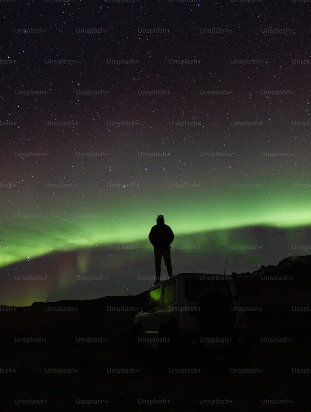 a person standing on a car with a green aurora in the background