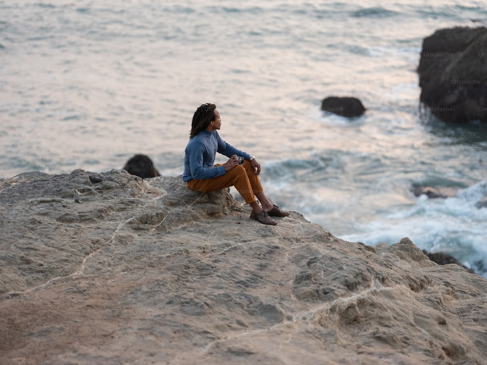Un homme assis sur un rocher au bord de l’eau