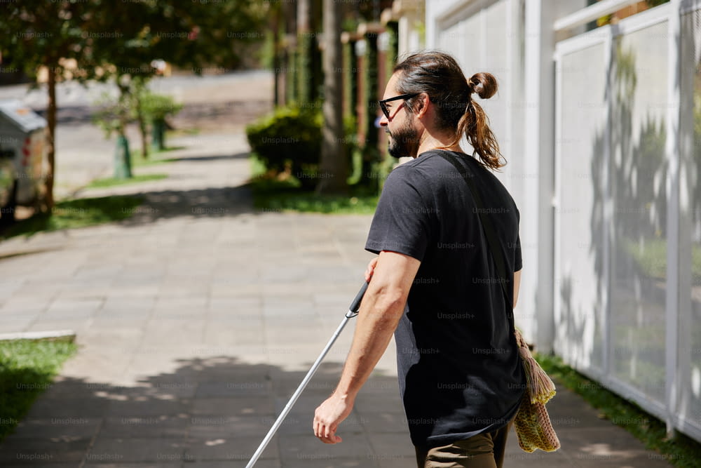 a man walking down a sidewalk with a stick in his hand