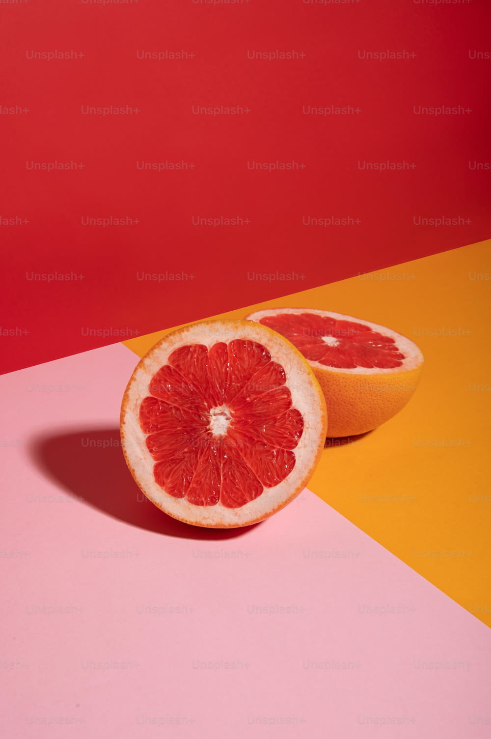a grapefruit cut in half on a pink and yellow background