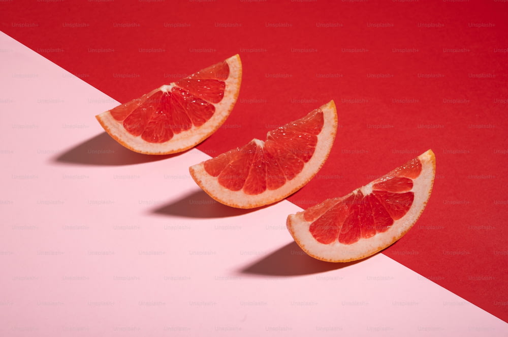 three slices of grapefruit on a pink and red background