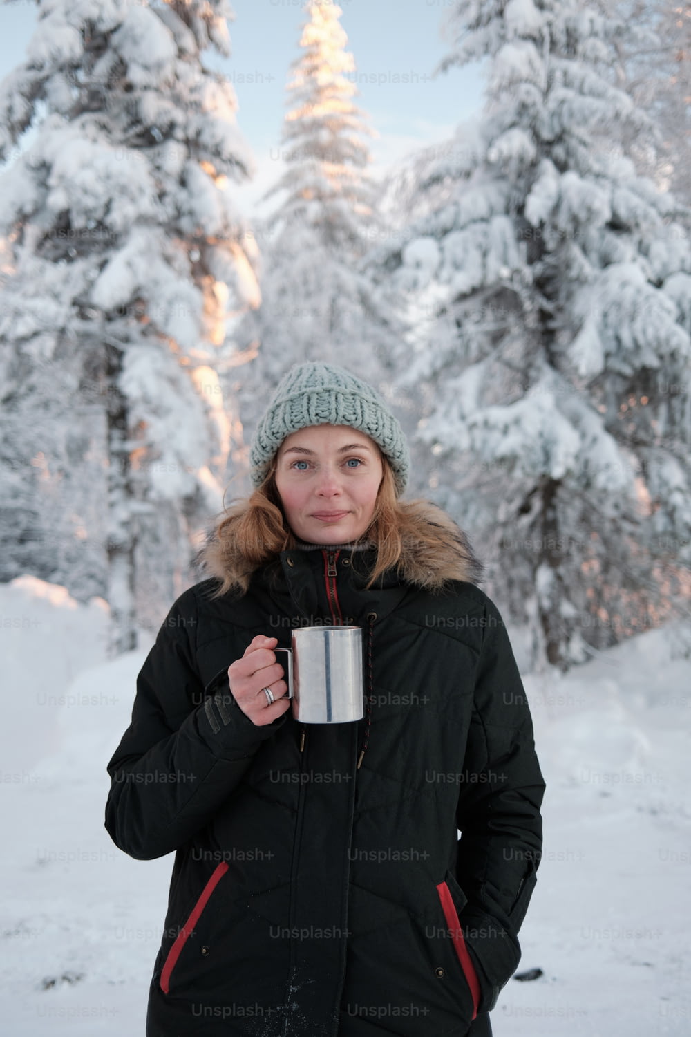 a woman standing in the snow holding a cup of coffee
