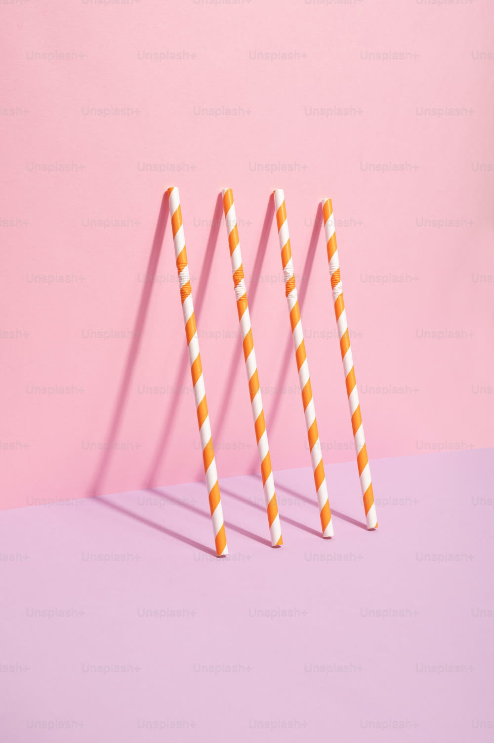 three orange and white striped straws on a pink background