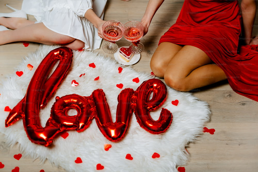 two women sitting on the floor holding glasses of wine with the word love spelled out