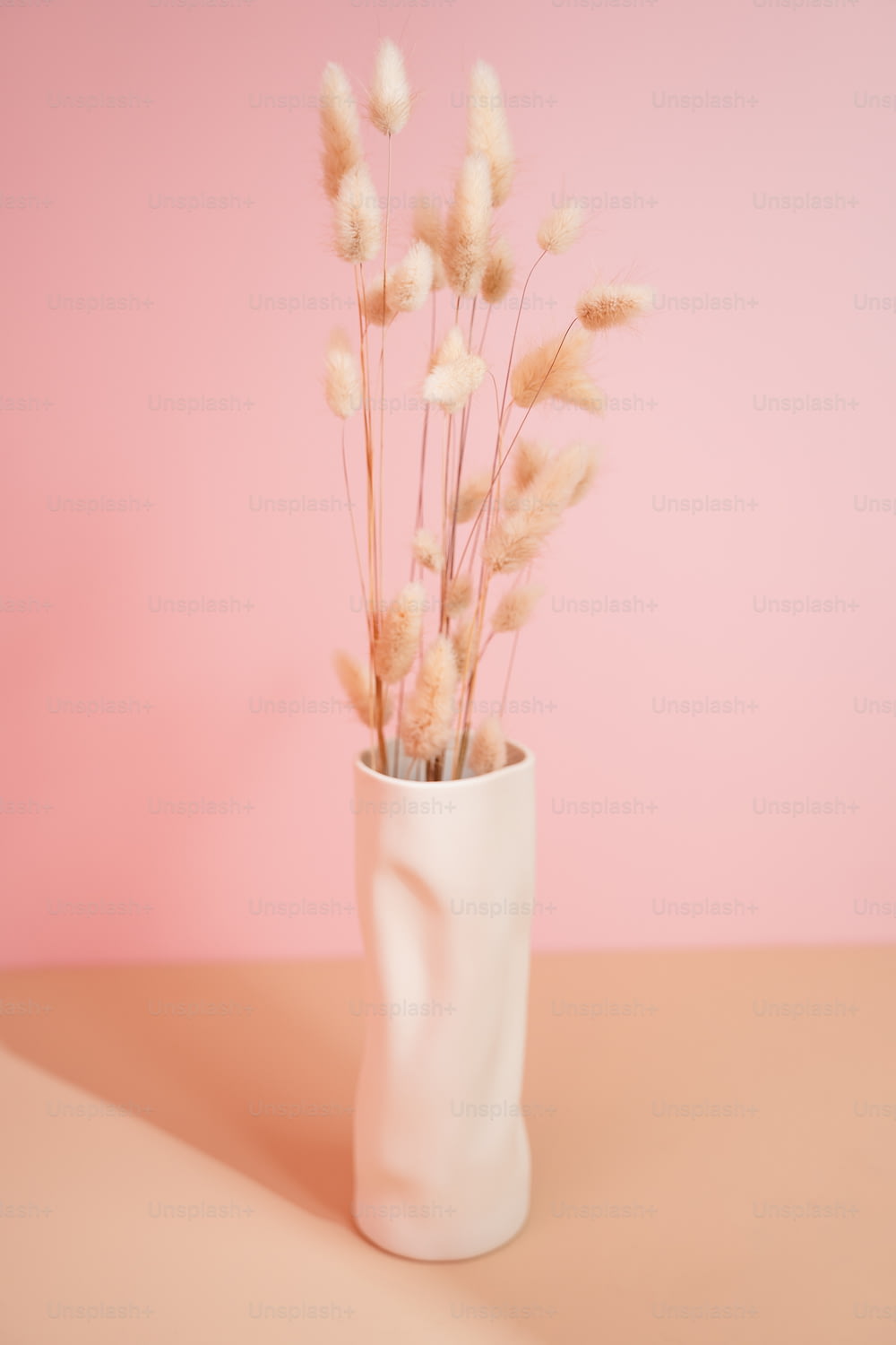 a white vase filled with dry grass on top of a table