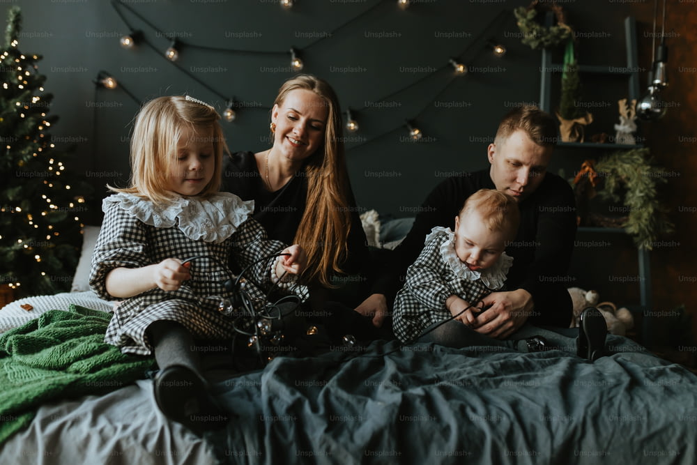 a family of three sitting on a bed in front of a christmas tree